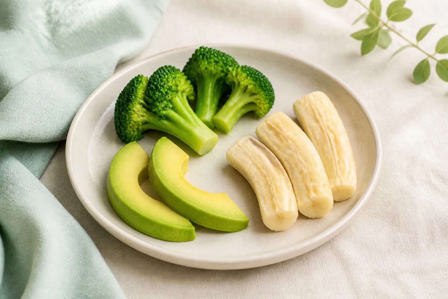 Soft finger foods on a small plate: broccoli spears, avocado and banana