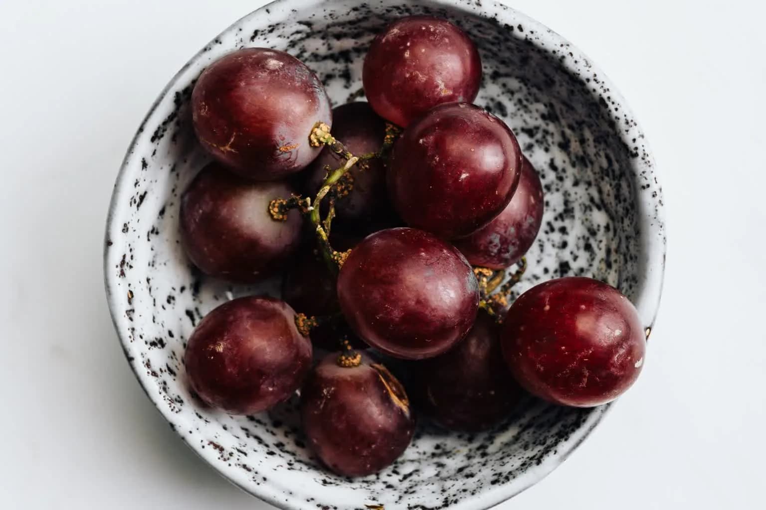 A small bowl of whole red grapes on a marble surface