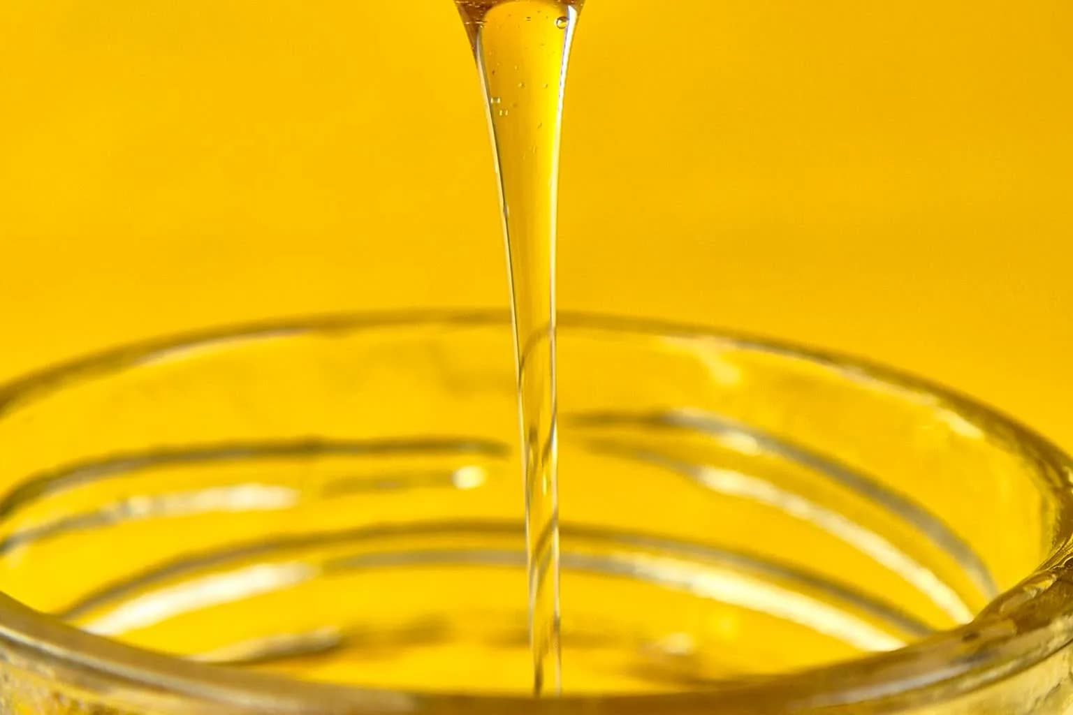 Honey drizzling from a dipper into a small glass jar