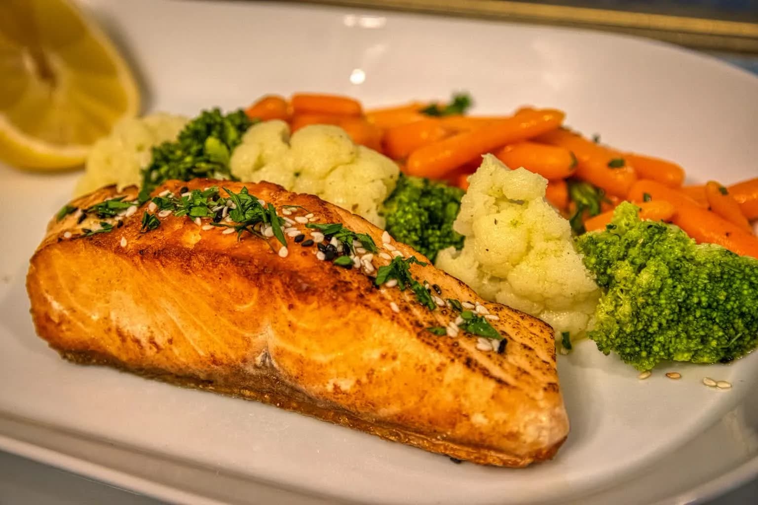 A cooked salmon fillet on a plate with steamed broccoli and carrots