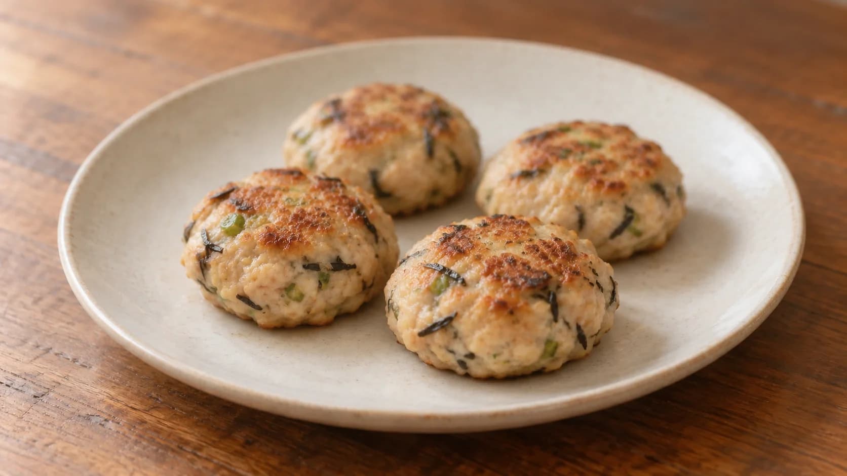 Four small browned chicken balls with kelp flecks on a plain plate