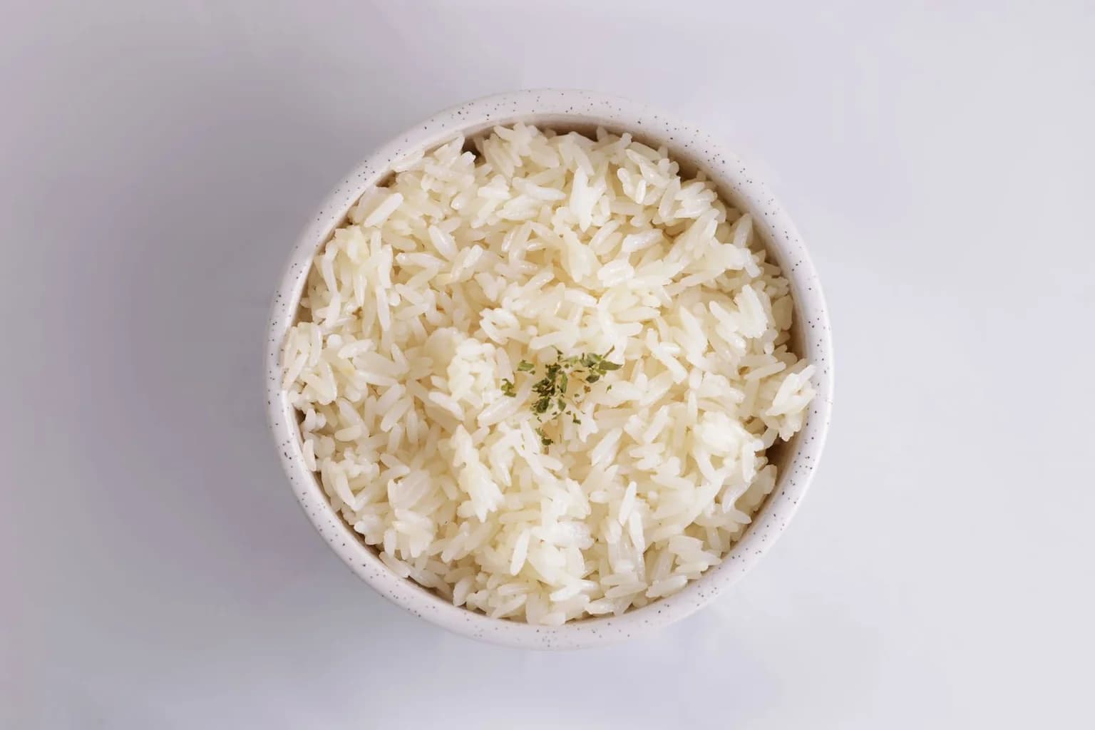 A speckled white bowl of fluffy cooked rice, seen from above